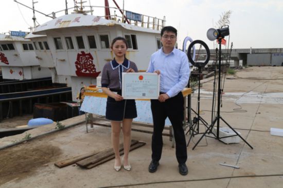 海鮮電商張夢琴與幫辦員手持食品經(jīng)營許可證合影。贛榆區(qū)委宣傳部供圖