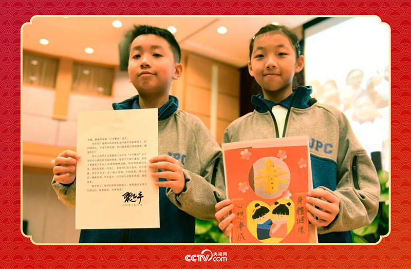 圖為香港“少年警訊”成員郭宏晞（左）展示習(xí)主席回信、羅顥凝（右）展示送給習(xí)主席的賀卡并合影。