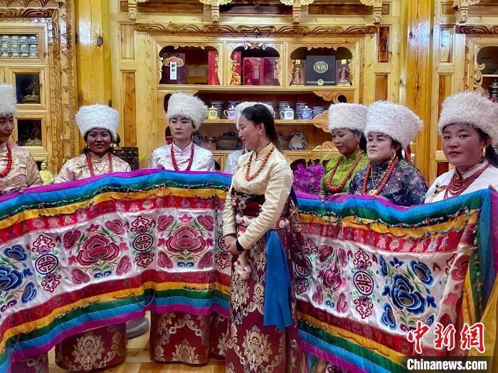 圖為女性展示村民自發(fā)繡制的“百米五彩哈達(dá)”?！±钣穹?攝